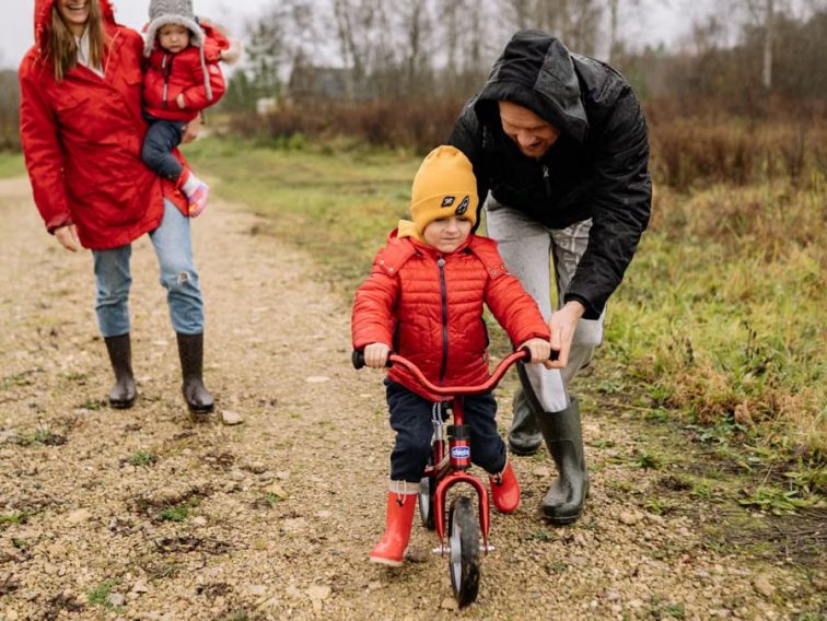 Happy family walking outdoors in fall, teaching child to ride bike.