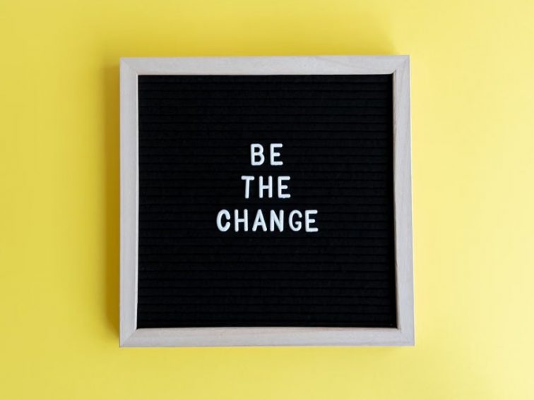 Minimalist letter board with 'Be The Change' quote on a vibrant yellow background.
