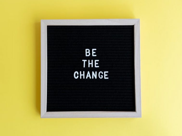 Minimalist letter board with 'Be The Change' quote on a vibrant yellow background.